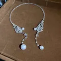 Detail view of an elegant rhinestone choker with pearl pendants on a brown velvet tray. - Symmetrical Wing Tassel Style / Silver