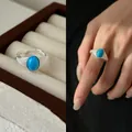 Nahaufnahme eines silbernen offenen Rings mit einem ovalen blauen Stein am Finger. - Silber