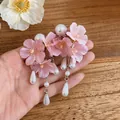 Close-up of pink fabric flower earrings with white pearl teardrop tassels in a hand - Pink