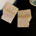 Close-up of geometric square layered earrings with iridescent rhinestones in high detail. - Gold
