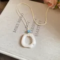 Detail of a minimalist resin ring pendant necklace on a cream cord with blue bead - Square / White