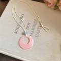 Close-up detail of pink resin ring necklace with blue bead on canvas book background - Round / Pink