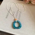 Close-up view of a minimalist teal resin irregular ring pendant on an off-white cord - Square / Green
