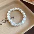 Detailed close-up showing white cat's eye stones and pearls on a rustic paper tray - Bracelet / White