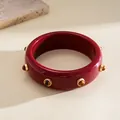 Detailed view of a retro red resin bangle with gold-colored metal studs and amber stones. - Red