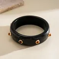Detail view of a retro black resin bangle with marbled texture and gold rivets. - Black