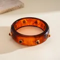 Close-up of vintage resin bangle featuring amber tortoiseshell pattern and gold rivets - Brown