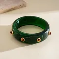 Detail view of a chunky dark green marbled resin bangle with golden decorative rivets - Green