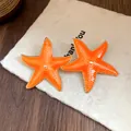 Close-up view of bright orange starfish stud earrings with a glossy drip oil finish. - Starfish Style (Silver Post) / Orange