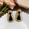 Close-up of geometric keyhole stud earrings in gold and black resin finish. - Hammered Irregular Geometric Style
