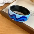 Close-up detail showing the vibrant blue wave print and smooth resin texture of the bangle. - Black & Blue