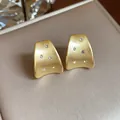 Macro view of minimalist matte gold brushed stud earrings with clear zircon inlays. - Gold