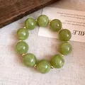 Detailansicht grüner Acryl-Rundperlen mit einzigartiger Wirbelstruktur und Gold-Abstandhaltern - Armband / Grün
