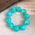 Nahaufnahme eines türkis marmorierten Acrylperlenarmband mit Goldakzenten auf Stoff - Armband / Himmelblau