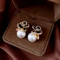 Close-up of elegant gold flower earrings with black petals and large white pearls - Gold-Black (Silver Pin)