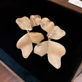 Close-up of elegant gold leaf-textured petal drop earrings on black velvet display - Gold