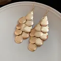 Detailed close-up of matte gold water-drop layered tassel dangle earrings on a plate. - Matte Teardrop Tassel / Gold
