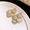 Close-up detail of gold dangle earrings featuring a blue and white floral oil print. - Earrings Only (Gold/Blue/White)
