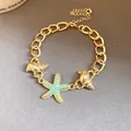 Detailed close-up showing gold chain bracelet with starfish and turquoise shell charms - Gold-Blue