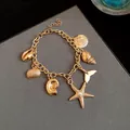 Close-up of gold charm bracelet featuring starfish, shell, and pearl ocean-themed pendants. - Bracelet-Starfish / Gold