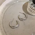 Detail view of silver twisted C-shaped stud earrings with micro-inlaid stones on ceramic plate. - Twisted Pleated C-Shape / Silver