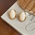 Close-up of vintage-style oval resin stud earrings featuring elegant gold-tone metal borders - Oval Studs / White