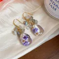 Detailed shot of handmade resin teardrop earrings with dried flowers and natural stones - Blue