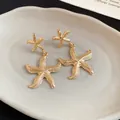 Close-up of the elegant gold wrinkled starfish pendant earrings with a textured finish. - Gold