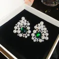 Close-up of elegant resin pearl earrings featuring a central green gemstone in a black box. - Silver Needle White Green