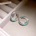 Close-up detail of silver-toned twisted hoop earrings with turquoise beads on a gray tray. - Huggie Earring - Blue
