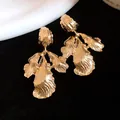 Close-up of vintage gold leaf pendant earrings with textured metal surface detail. - Gold