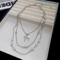 Dettaglio di un'elegante collana d'argento multistrato con perle e ciondoli a croce - Argento