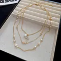 Primo piano di una collana multistrato dorata con perle e ciondolo a croce di strass - Oro