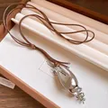 Vista dettagliata di un ciondolo a conchiglia d'argento su una collana di corda - Stile Ciondolo a Conchiglia / Argento Con Corda Caffè