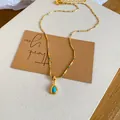 Nahaufnahme einer eleganten vergoldeten Halskette mit blauem Tropfenanhänger auf weißem Stoff. - Wassertropfen Anhänger Halskette (HN12608) / Gold-Blau
