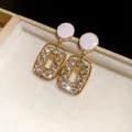 Detailed macro view of elegant gold-tone hollow square drop earrings with sparkling crystals. - Gold-White