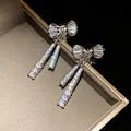 Close-up of sparkling zirconia bow-knot earrings with tassel detail on a jewelry box. - Clip-On Earrings / Silver
