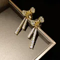 Close-up of elegant gold bow clip-on earrings with shimmering zircon tassel drops - Clip-On Earrings / Gold