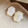 Vista detallada de elegantes pendientes ovales de resina con marco metálico dorado - Blanco