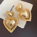 Close-up of gold glossy heart drop earrings showing retro metallic texture - Gold