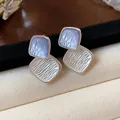 Makro-Detailansicht der strukturierten blau-weißen Emaille-Ohrstecker auf dem Display - Doppelraute Emaille-Stil / Silber-Lila