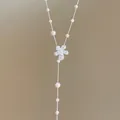 Nahaufnahme von funkelndem Blumenanhänger und weißer Perlen-Quastenkette - Blumen-Quasten-Stil / Weiß