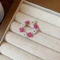 Gros plan d'une bague artisanale en perles de verre aux motifs floraux roses et blancs délicats - Bague / Rose rouge