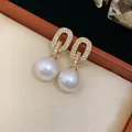 Close-up of elegant gold zircon oval earrings with large white pearl drops - Oval Pearl Drop Style / Gold