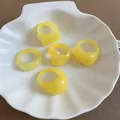 Close-up of yellow resin rings set in various geometric and wavy shapes in a white shell dish - 5 Pieces / Yellow