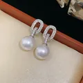 Elegant detail of silver-tone oval stud earrings with pavé zircons and large white pearls - Oval Pearl Drop Style / Silver