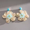 Close-up view of handmade woven raffia flower earrings with light blue fabric centers - Blue