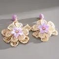 Detailed view of hand-woven raffia flower earrings with purple fabric petals. - Purple