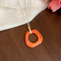 Dettaglio di un ciondolo geometrico in acrilico arancione su una collana in corda di pelle bianca - Pendaglio Quadrato / Arancione