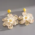 Detailed close-up of handmade woven raffia flower earrings for a summer vacation look - Yellow